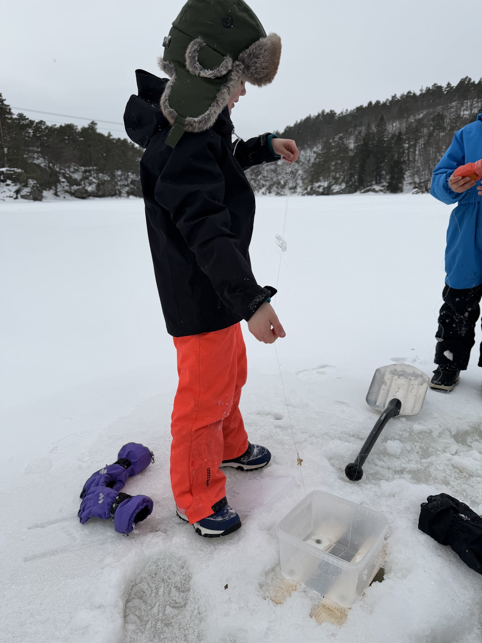 A child ice fishing on a frozen lake during a winter cabin-to-cabin journey