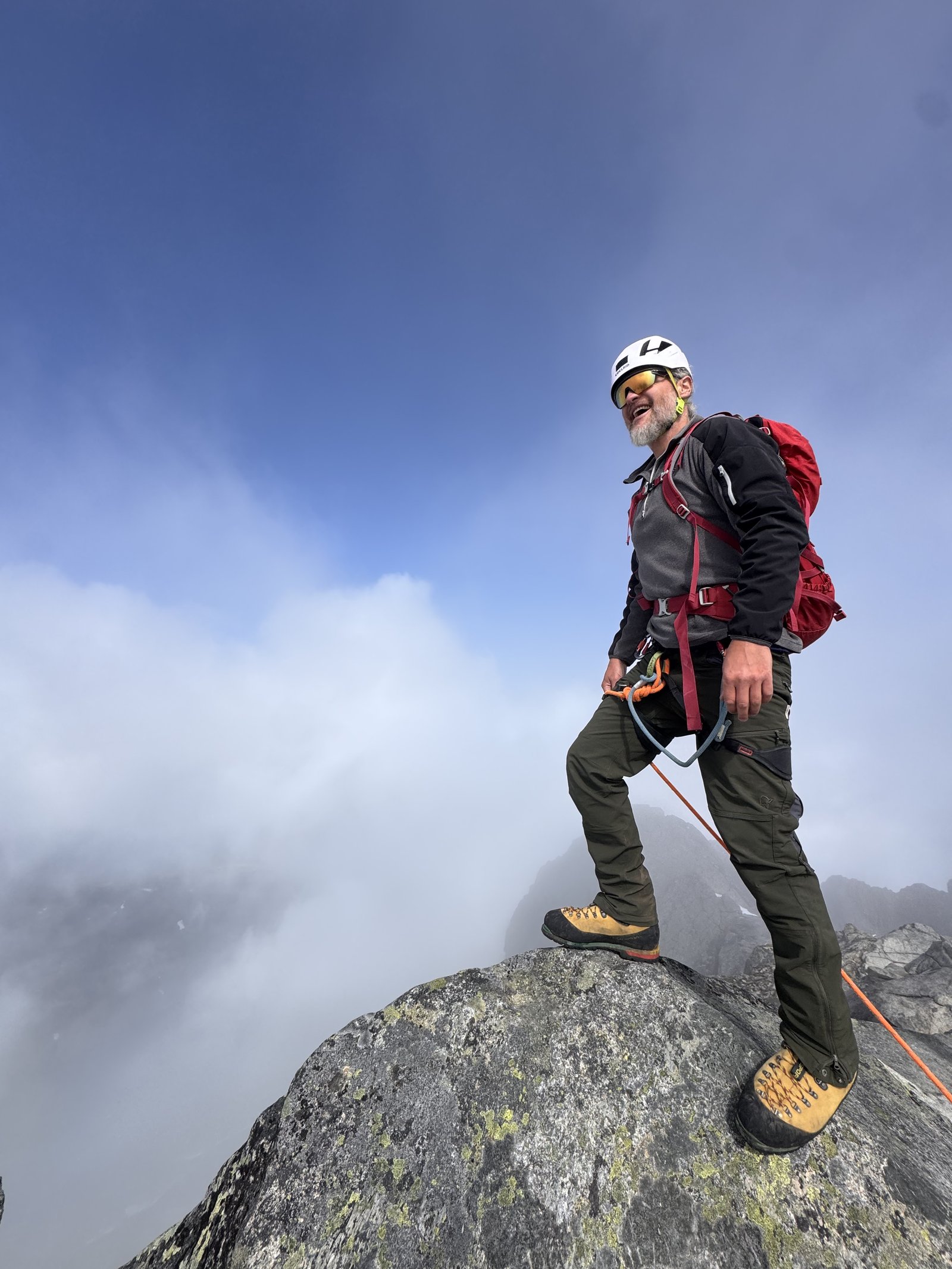 A climber standing on the summit rock of Storen, Jotunheimen, with clouds below